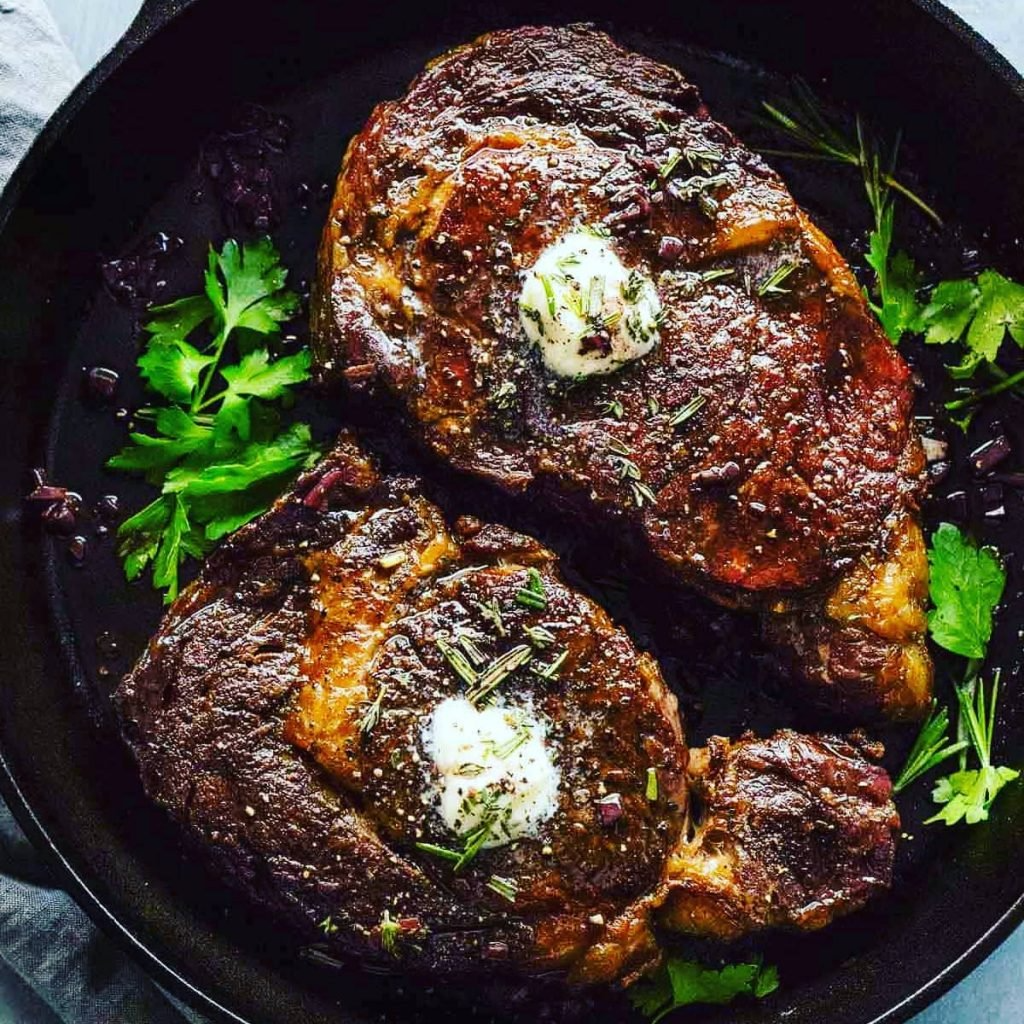 two seared steaks in a cast iron pan with butter and herbs