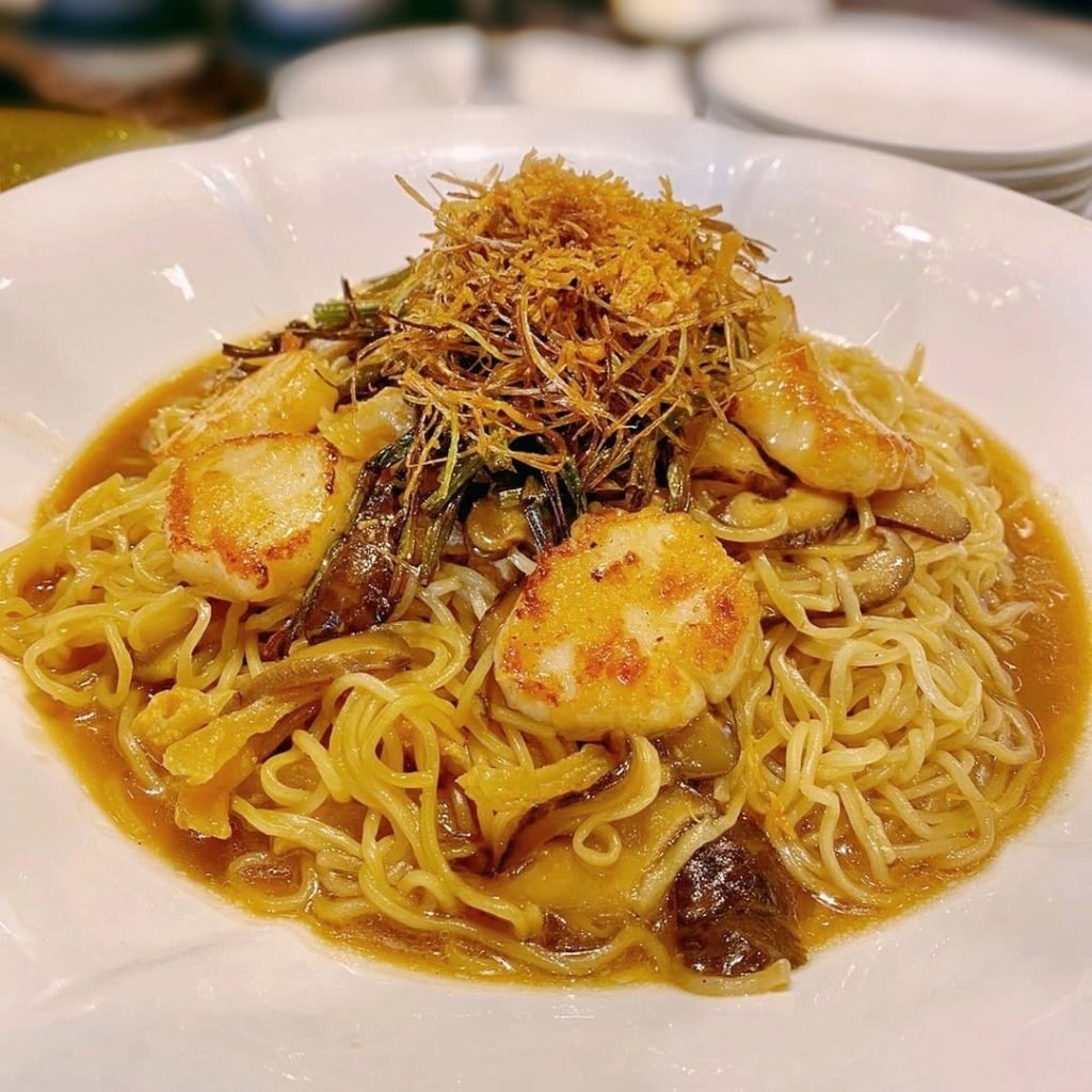 A white bowl from Black Society featuring yellow egg noodles tossed in a savory brown sauce