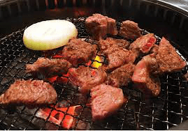 Close-up of cubed meat and a slice of onion grilling on a wire mesh over glowing charcoals at Chang Korean Charcoal BBQ Restaurant