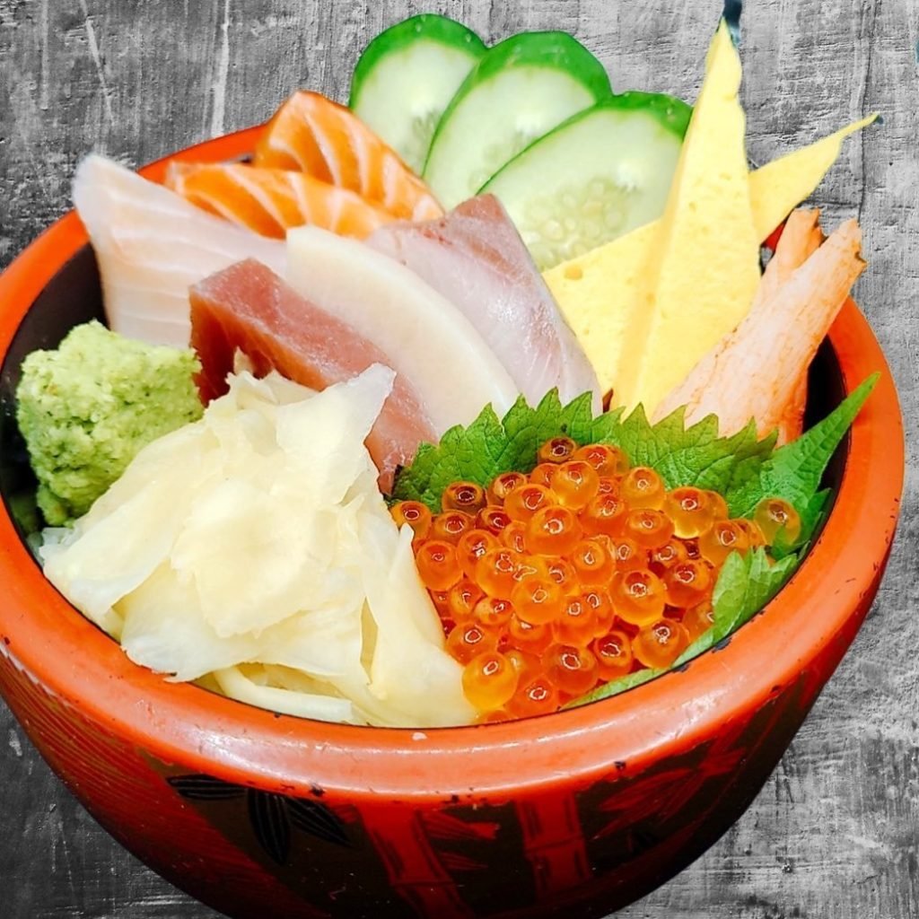 A vibrant chirashi don from Himawari Japanese Restaurant, served in a traditional red and black lacquered bowl over sushi rice.