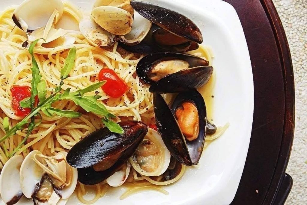 A close-up of a white plate from Old Habits Cafe featuring spaghetti tossed with fresh clams and mussels in their shells.