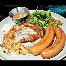 Platter with roasted pork belly, two large sausages, rosti or hash browns, salad, and gravy.