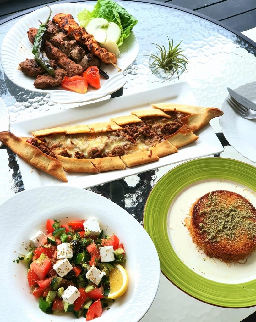 A spread of Turkish dishes from Arkadas Cafe & Restaurant on a glass-topped outdoor table, featuring a mixed grill platter with chicken and meat kebabs