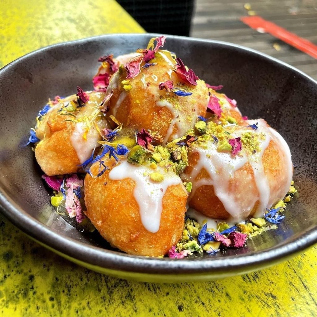 A close-up shot of a dessert from Artichoke Singapore, featuring Loukoumades (fried dough balls) drizzled with white glaze