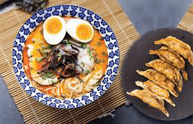 Overhead view of a bowl of ramen with soft-boiled egg and a side plate of pan-fried gyoza on a bamboo mat