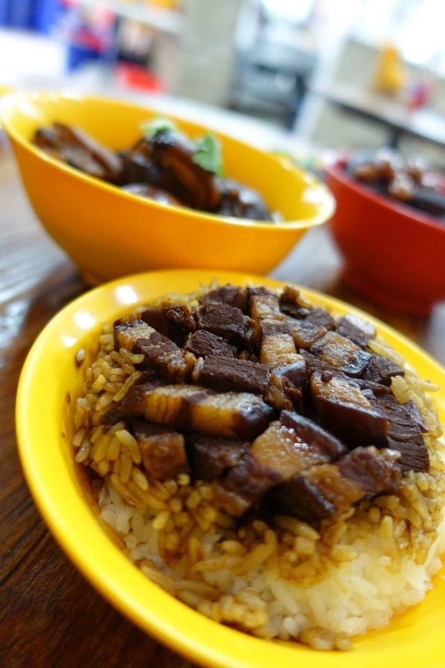 Close-up of a bright yellow bowl from Authentic Mun Chee Kee King of Pigs Organ Soup, filled with white rice topped with savory braised pork belly pieces and sauce