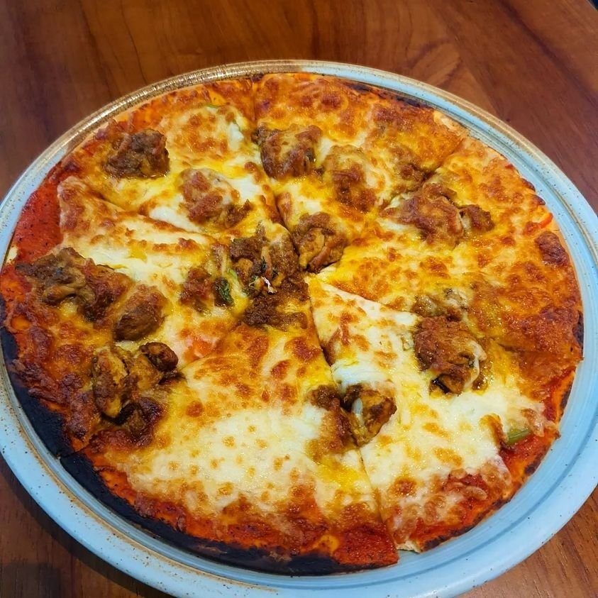 Close-up overhead view of a sliced chicken tikka pizza from Bacos