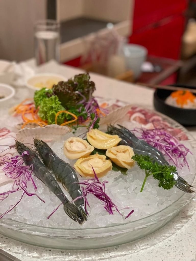 A large glass platter from Beauty in The Pot, filled with crushed ice and an assortment of fresh raw seafood for hotpot.