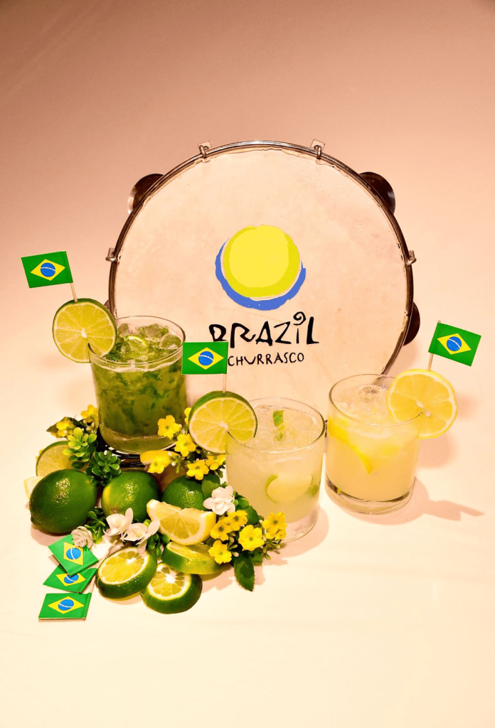 Three Brazilian Caipirinha cocktails with lime, lemon, and Brazilian flags, displayed with a Pandeiro drum for 'Brazil Churrasco'