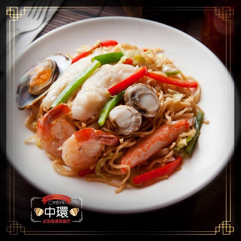 Promotional image for Central Hong Kong Cafe showing a white plate of stir-fried seafood noodles topped with prawns, scallops, fish fillet, a mussel, crab stick, and mixed bell peppers.