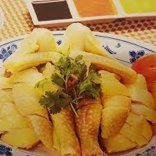 Plate of sliced Hainanese poached chicken with coriander garnish and dipping sauces in the background