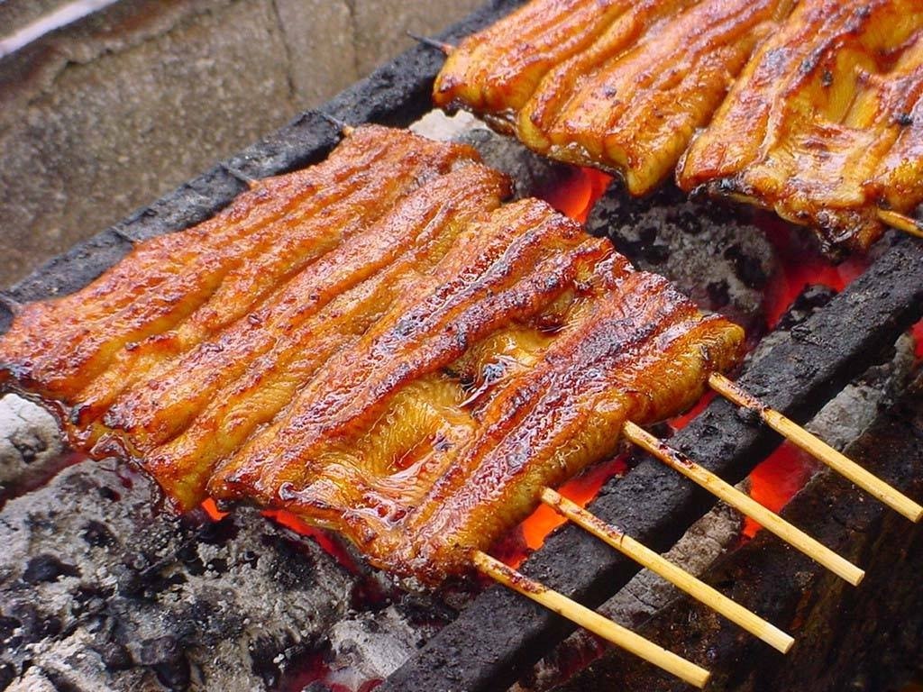 Close-up of glazed and charred unagi (eel) fillets on bamboo skewers grilling over glowing red hot charcoal at Chikuyotei Japanese Restaurant