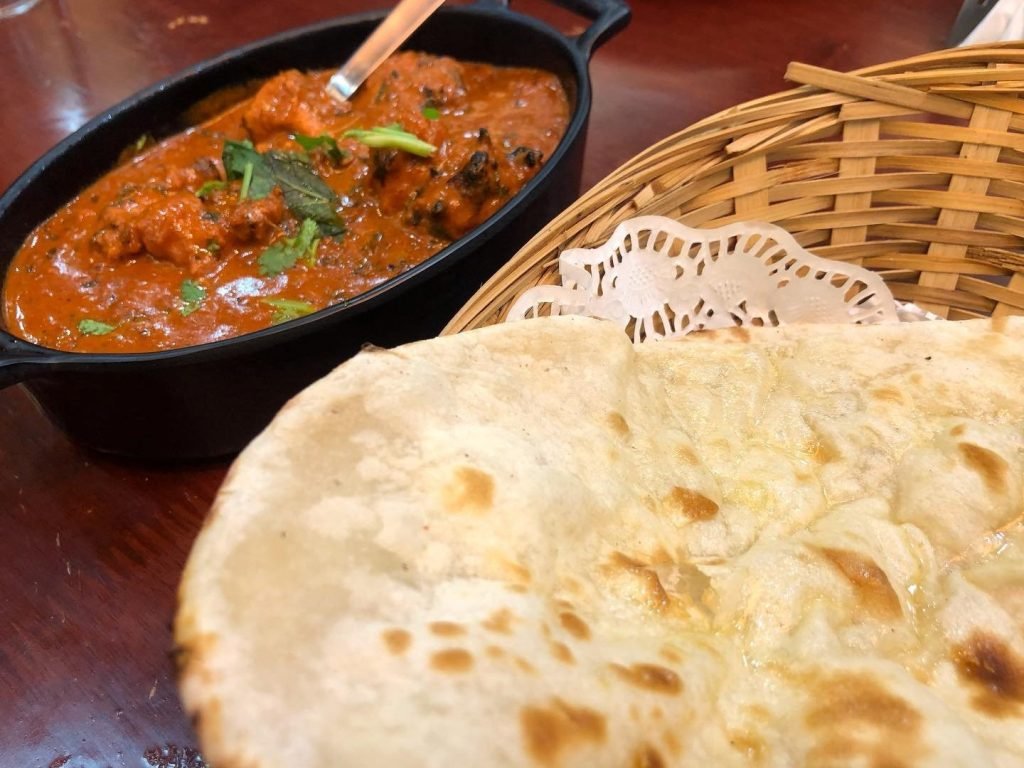 Meal from Curry Bowl featuring a black oval dish of creamy, reddish-orange Indian chicken curry