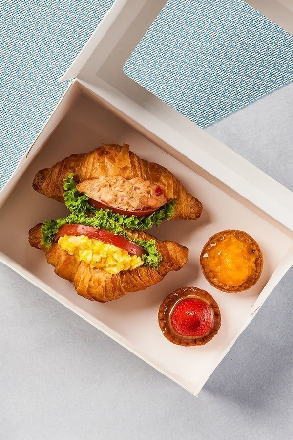 An open white takeaway box from Delifrance containing two croissant sandwiches