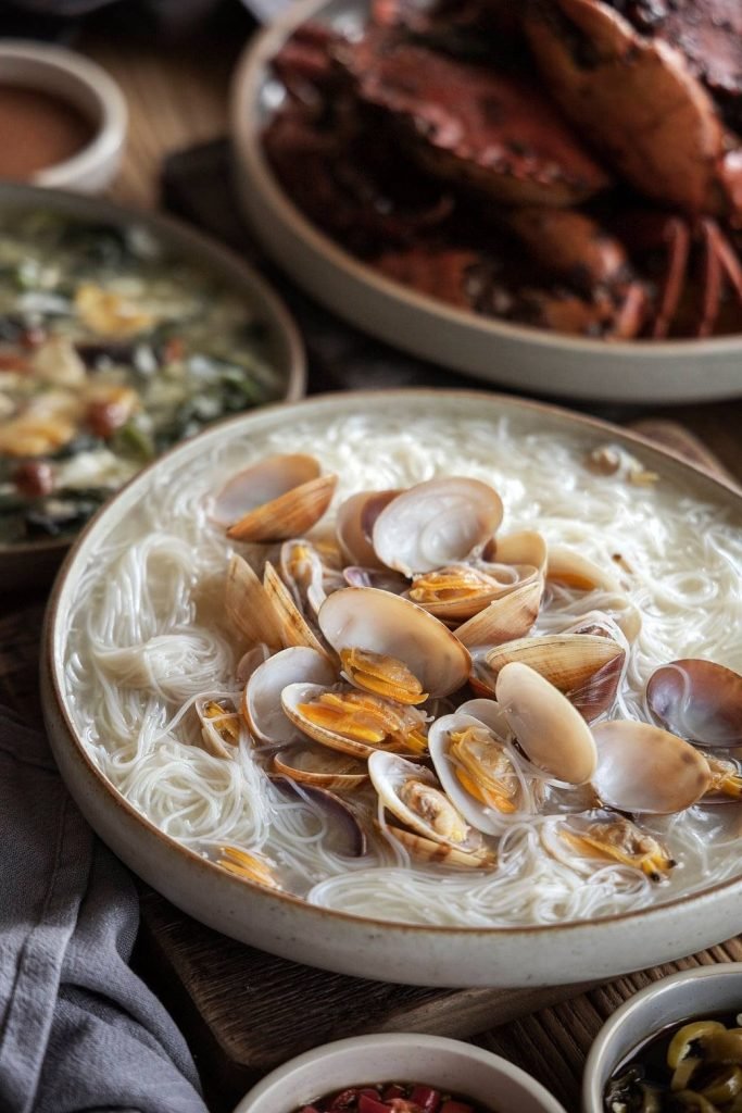 A close-up of a large rustic ceramic bowl filled with lala white bee hoon (clams with rice vermicelli noodles) from Diamond Kitchen.