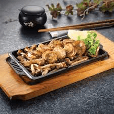 Japanese-style grilled mushrooms served on a traditional hot plate, accompanied by a lemon slice and chopsticks.