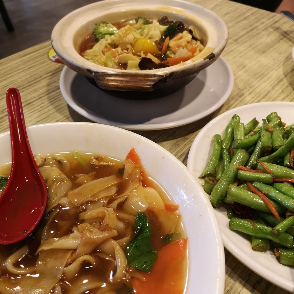 A vegetarian meal from Forest Dew Restaurant, featuring a bowl of flat rice noodles in gravy, a claypot of mixed vegetables, and a side of stir-fried green beans