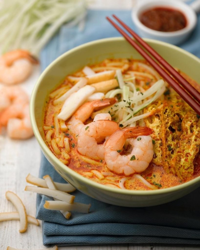 A tempting bowl of laksa from Fortune Food Geylang Bahru, served in a light green bowl with red chopsticks.
