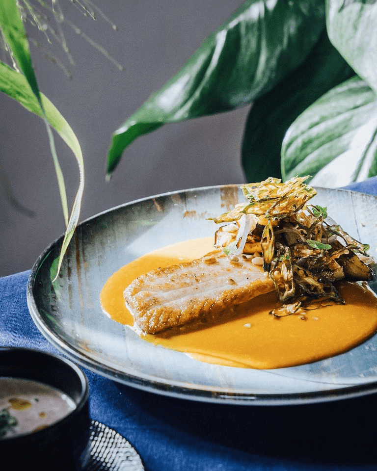 Elegantly plated pan-seared fish fillet resting on a vibrant orange sauce, accompanied by a garnish of crispy fried vegetables