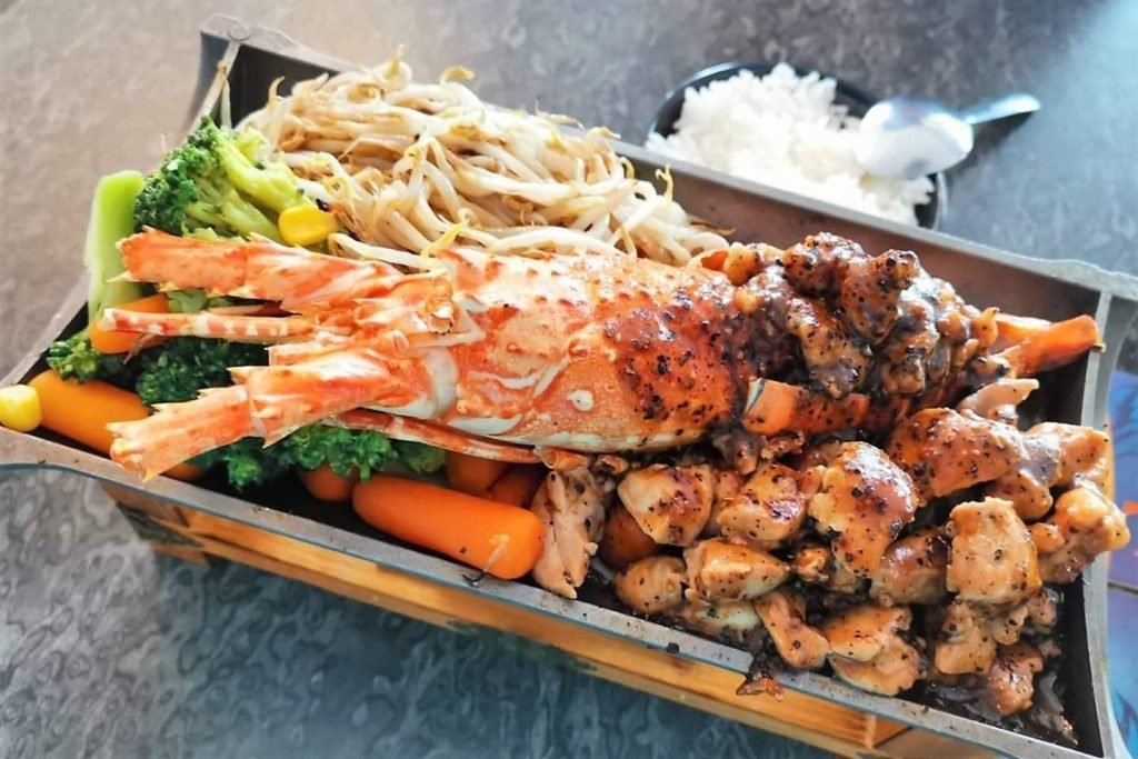 A teppanyaki platter from Haven Bistro Taiwanese Teppanyaki, featuring a grilled lobster, diced black pepper chicken, bean sprouts, broccoli, and carrots, served with a side of rice