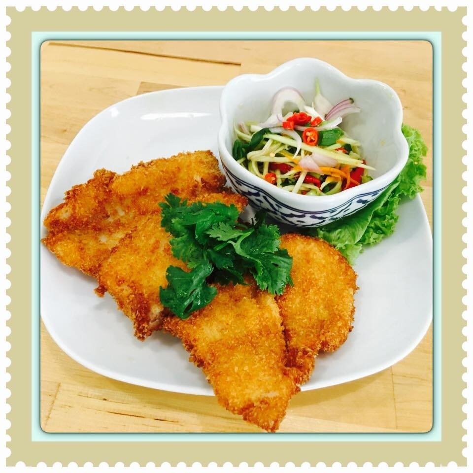 Crispy fried fish fillets from Nangfa Thai Kitchen, served with a side of Thai green mango salad, garnished with cilantro on a white plate