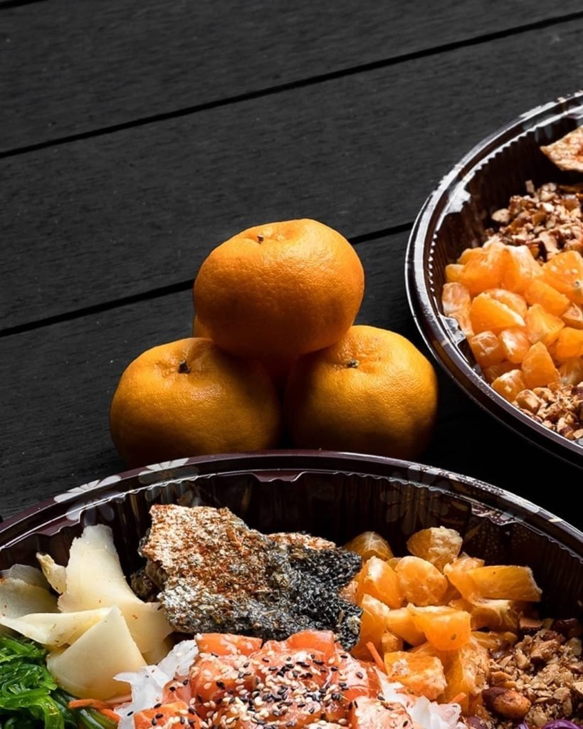 Two Poke Theory poke bowls with a Chinese New Year theme, including salmon, crispy skin, and mandarin orange segments, with a stack of three mandarin oranges placed between them on a dark wooden background.