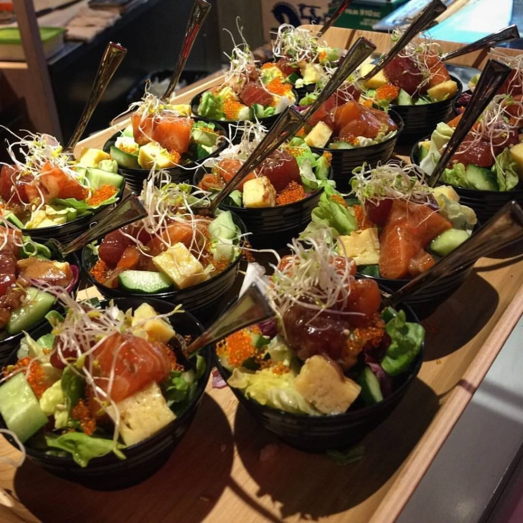 A wooden tray holding multiple small black bowls filled with Japanese-style sashimi salad