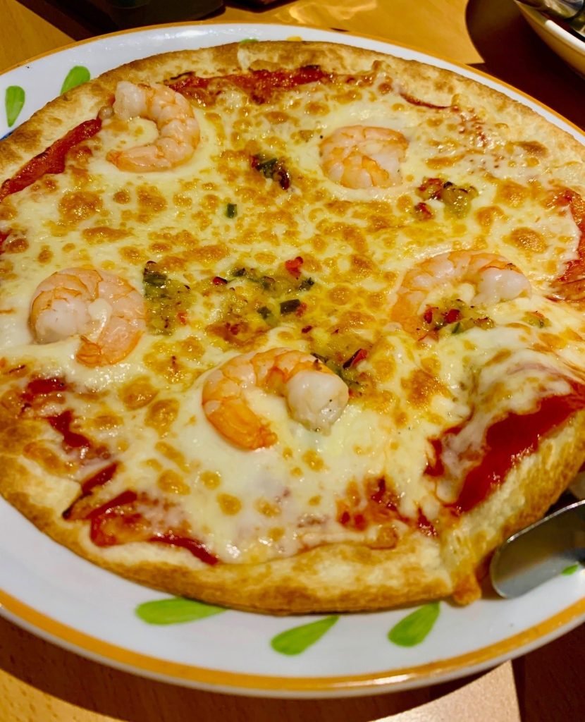 A whole pizza topped with cooked shrimp, melted mozzarella cheese, and tomato sauce, served on a white plate with a yellow and green patterned rim