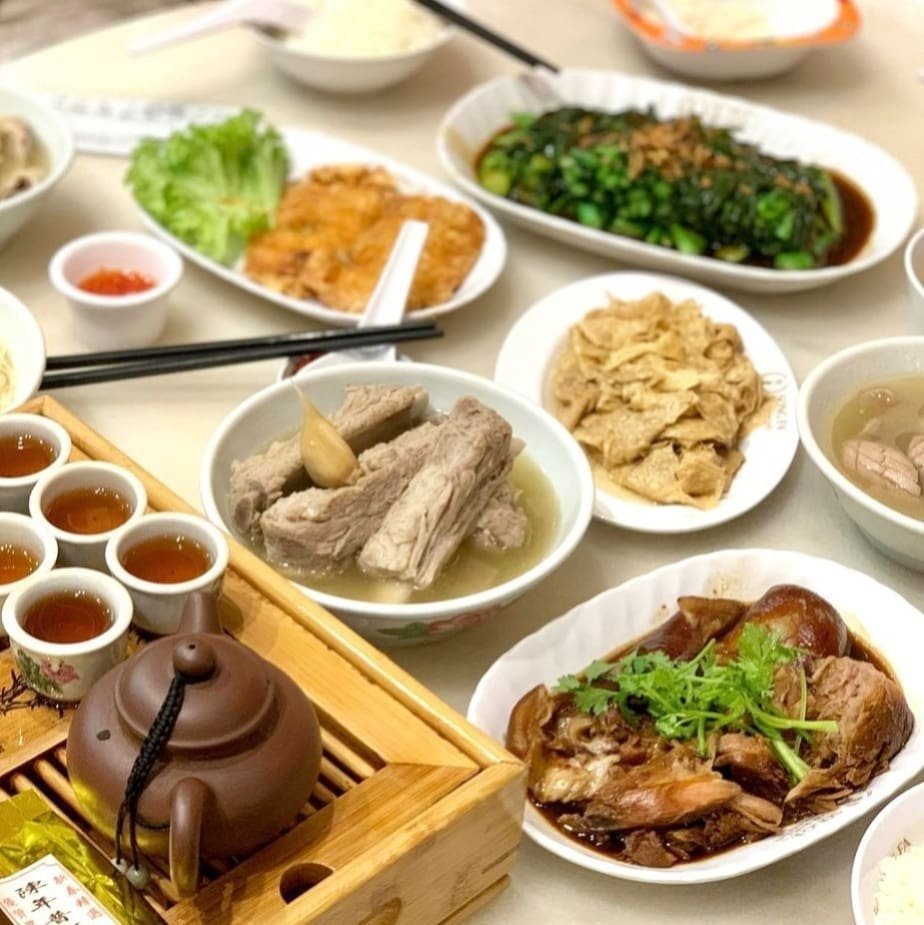 A table laden with a variety of Asian dishes, including a bowl of Bak Kut Teh