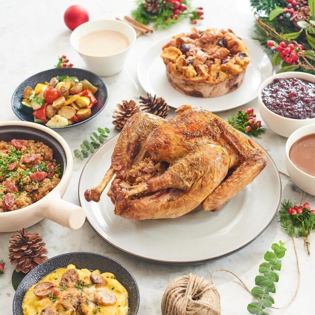A beautifully arranged holiday feast with a roast turkey, sausage mac and cheese, roasted vegetables, a sausage and rice dish, bread pudding, cranberry sauce, gravy, and a festive drink