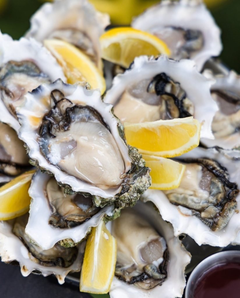 Platter of fresh raw oysters served with lemon wedges and dipping sauce.