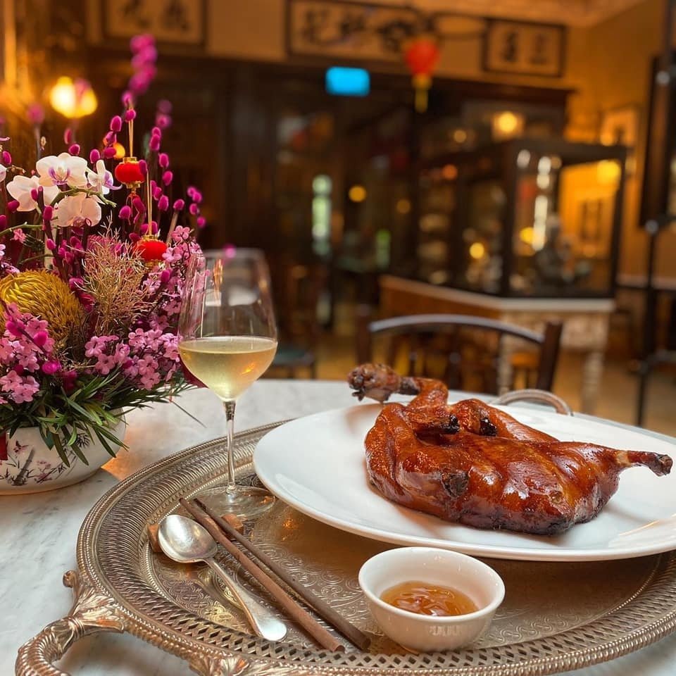 Festive roasted duck dinner with wine and flowers on a silver tray in a Chinese restaurant.
