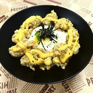 Fried chicken and egg rice bowl with cheese sauce, seaweed, and sesame seeds in a black bowl.