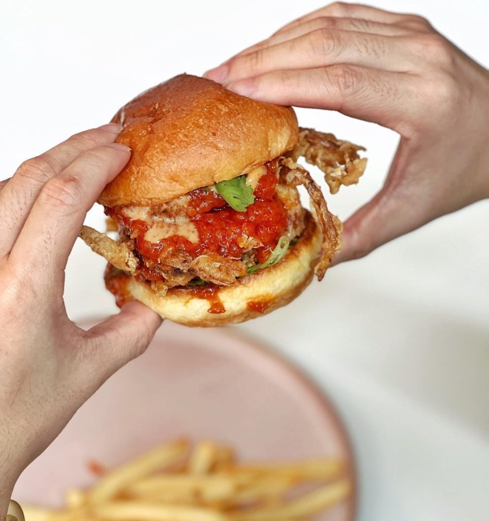 A person holding a juicy soft-shell crab burger from The Refinery