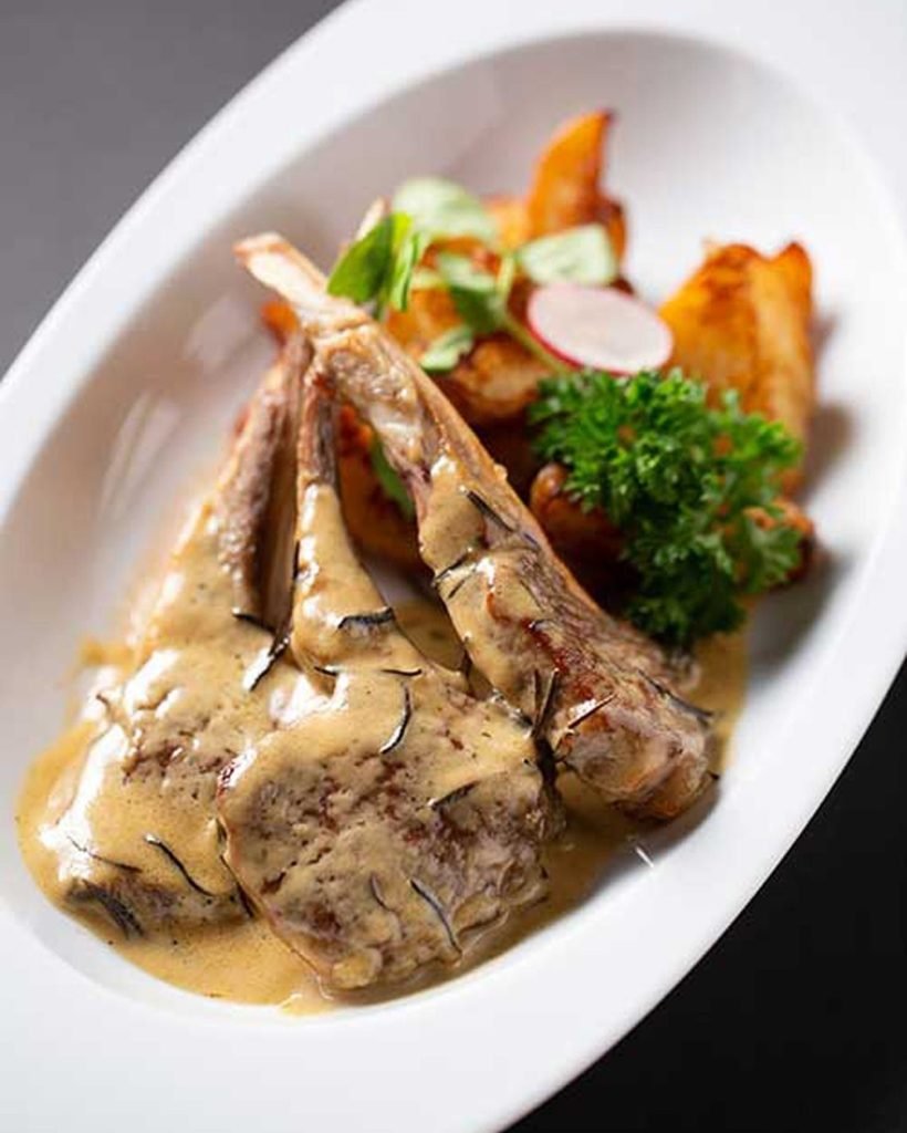 Plated lamb chops in creamy sauce with roasted potatoes and fresh garnish