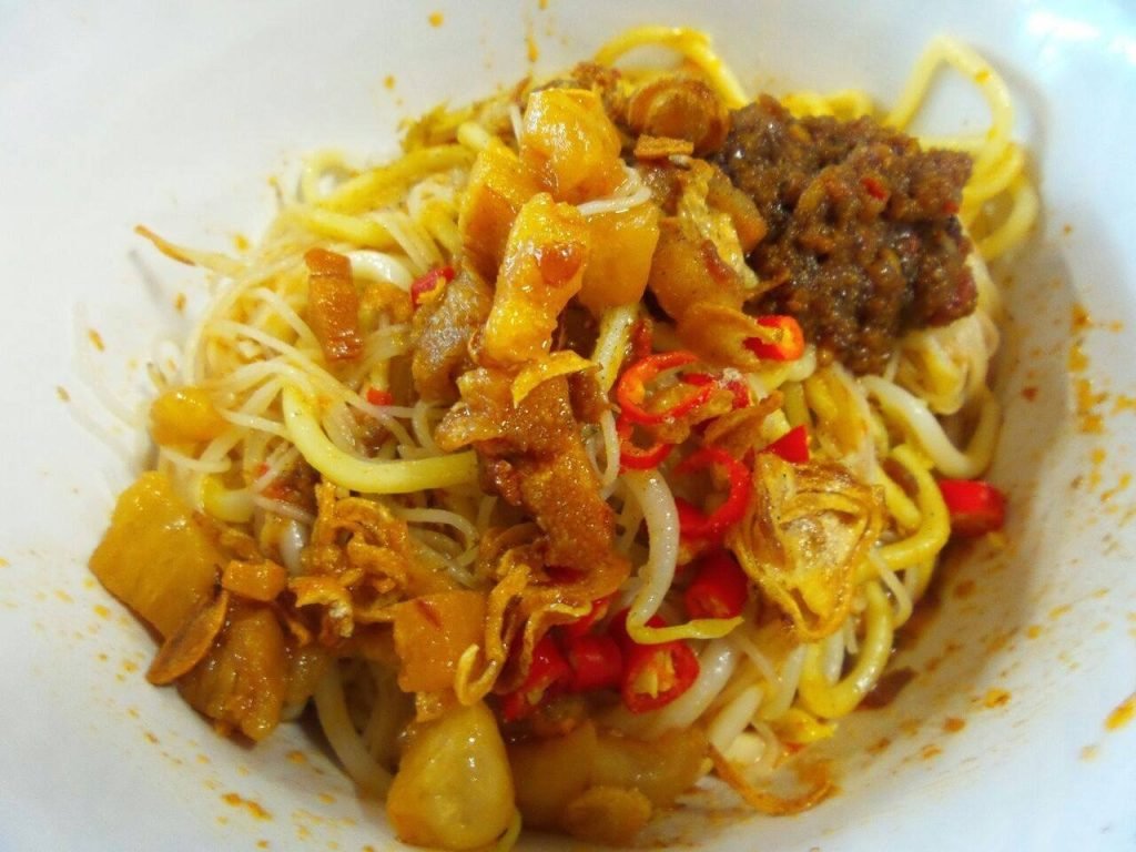Close-up of fried Hokkien Mee noodles with various toppings including chili paste, pork lard, and fresh chilies
