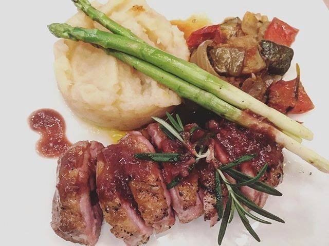 Plated seared duck breast with mashed potatoes, asparagus, roasted vegetables, and sauce