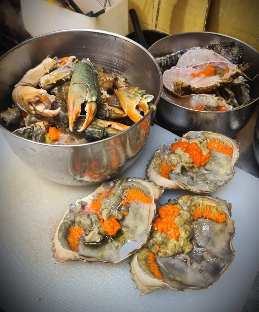 Fresh crabs being prepared at 新福记 Xin Fu Ji, showing crab claws in a metal bowl and several crab carapaces filled with bright orange roe on a cutting board