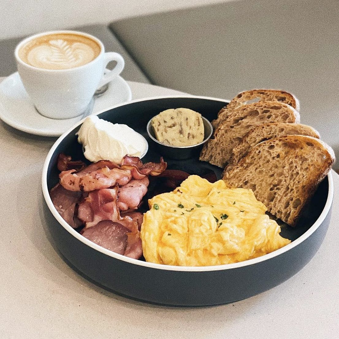 Breakfast plate with scrambled eggs, bacon, toast, spreads, and a cup of coffee