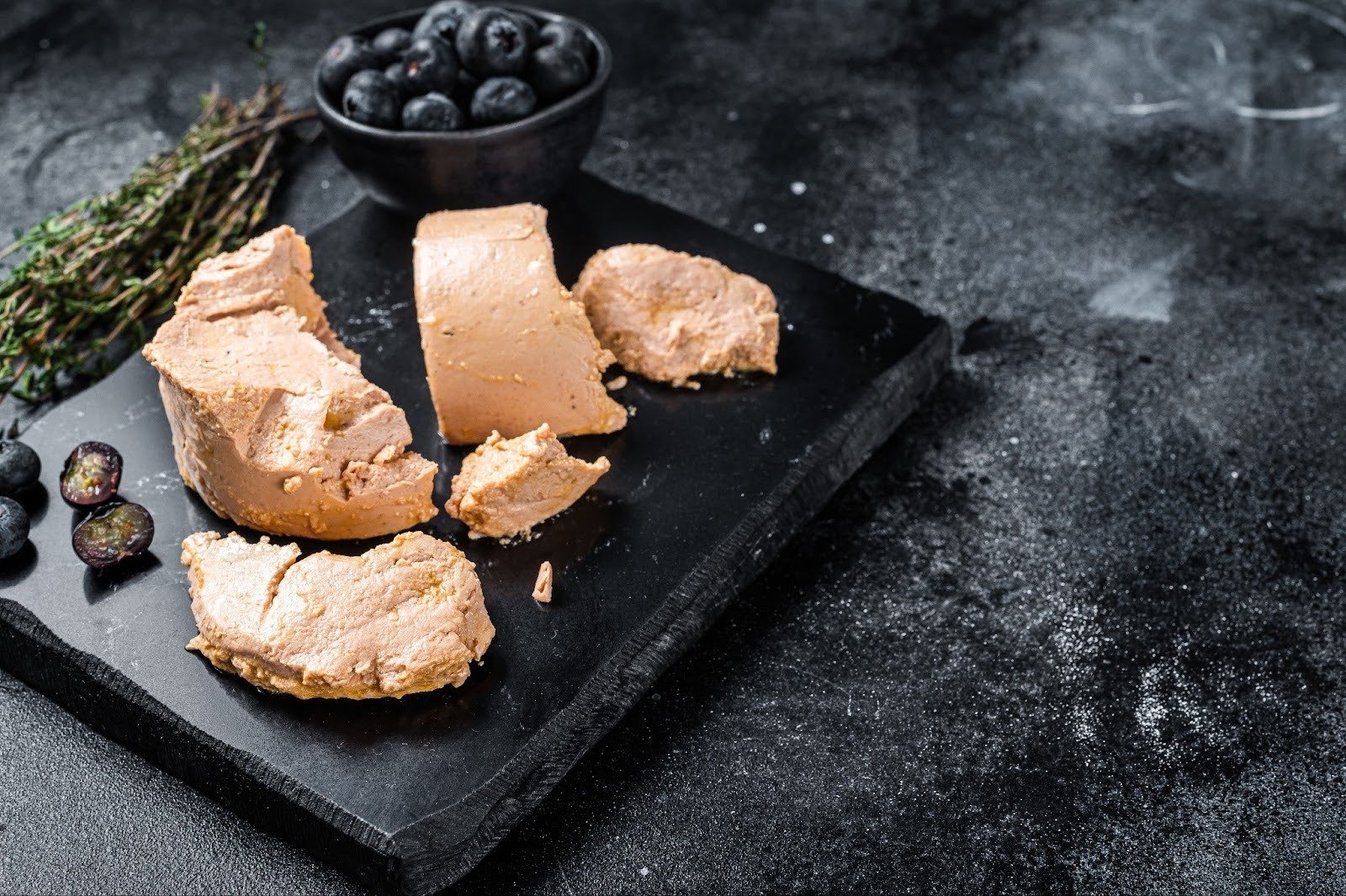 Foie gras pâté served on a slate board with fresh blueberries and thyme