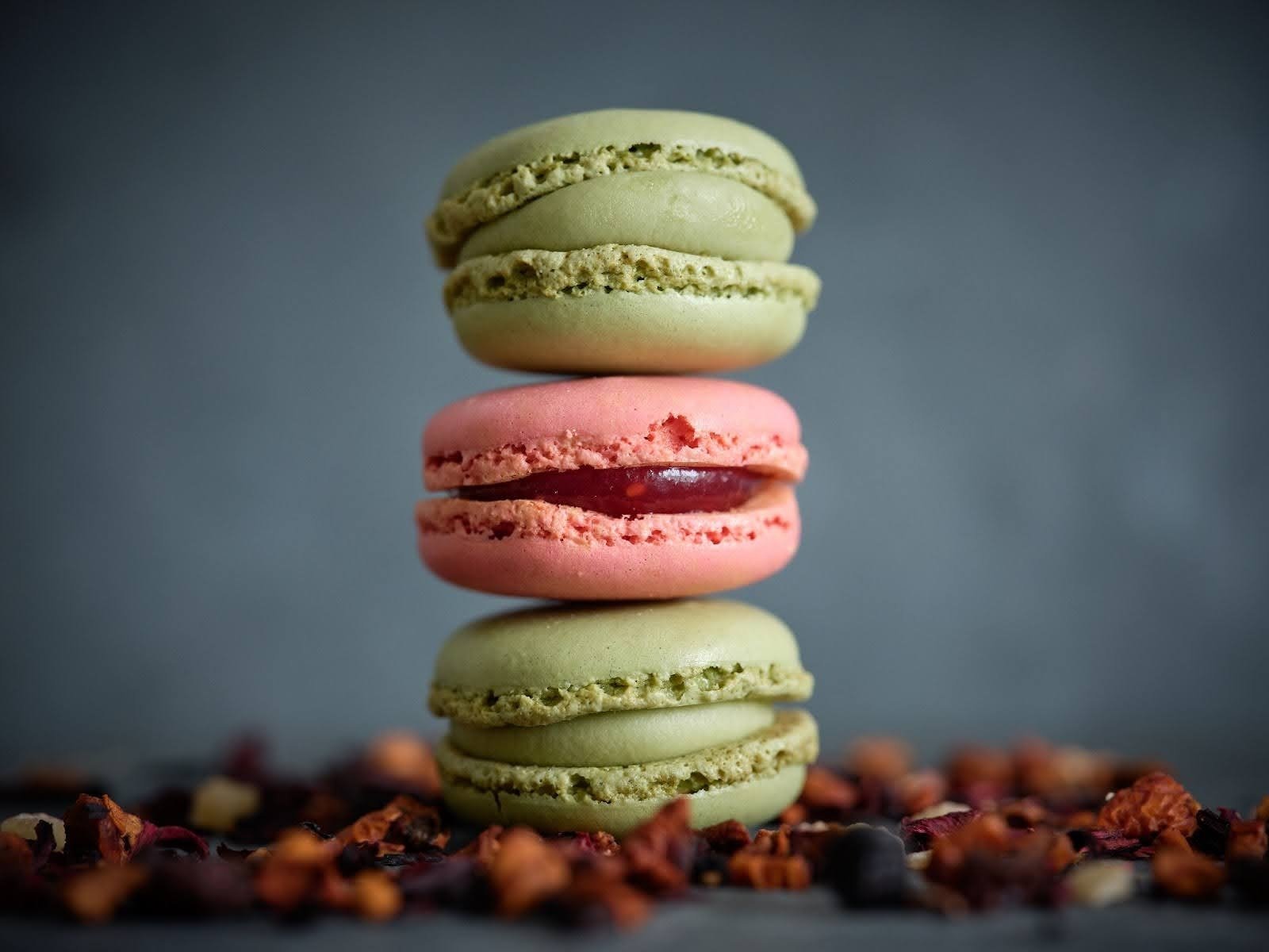 A stack of three colorful French macarons on a dark background