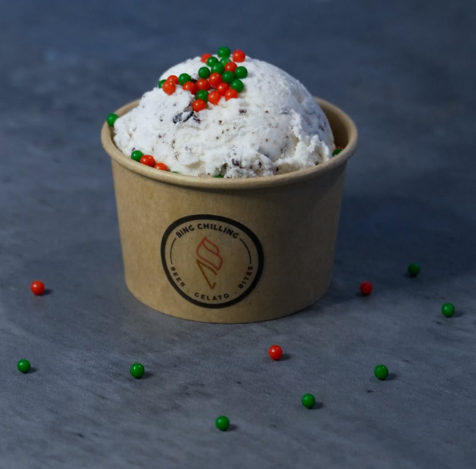 A cup of gelato from Bing Chilling, topped with festive red and green sprinkles on a grey surface