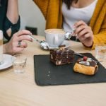 Two women sitting at a cafe table, sharing a slate platter with a brownie and a pastry while enjoying their coffee drinks