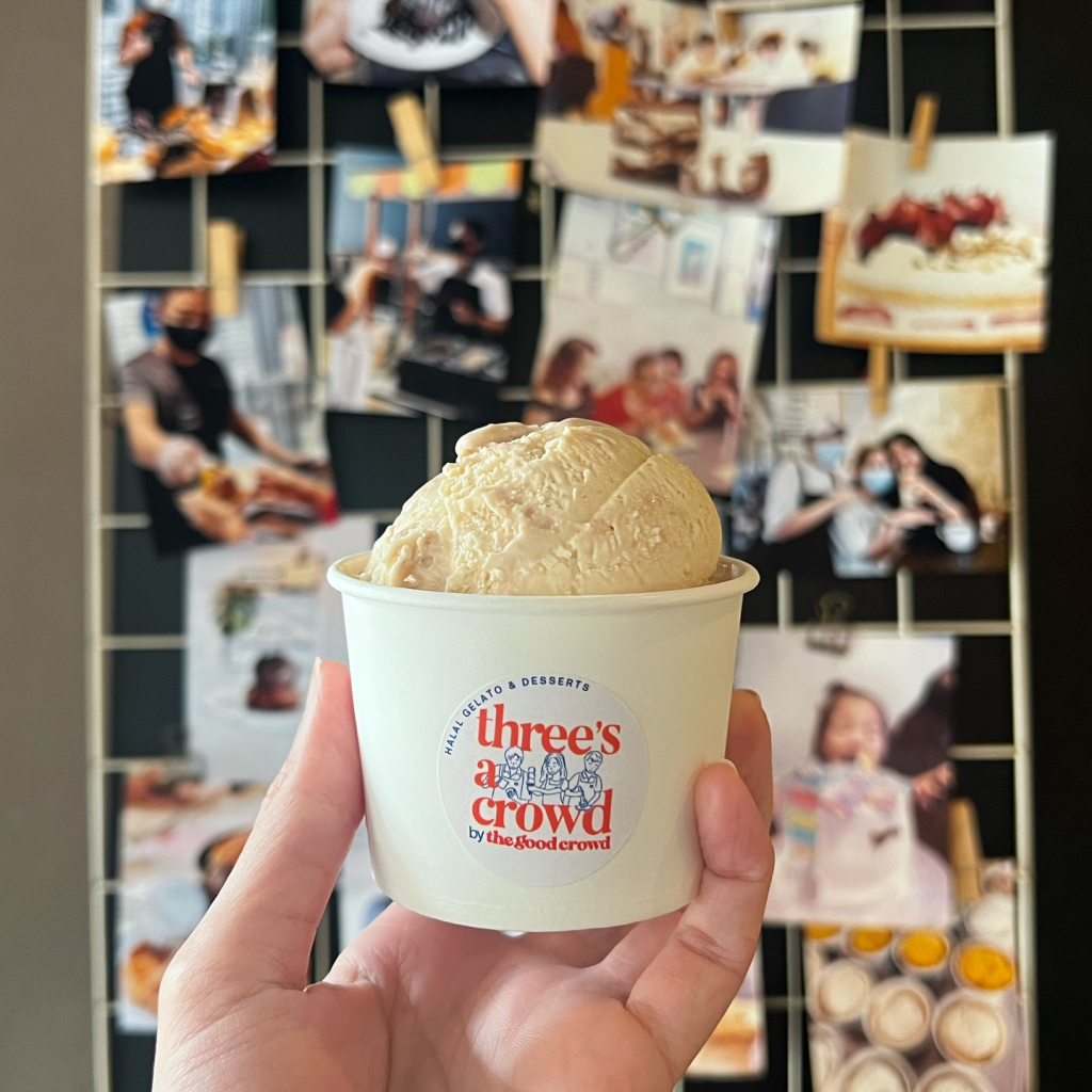 A person's hand holds up a white paper cup with a scoop of gelato