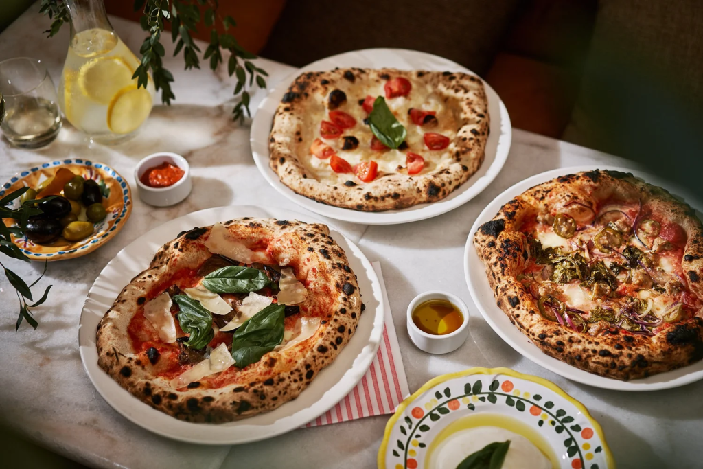 Three authentic Neapolitan wood-fired pizzas with charred crusts served on a marble table at Cicheti