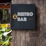 A modern minimalist Bistro & Bar sign mounted on a rustic wooden pillar