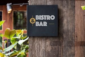 A modern minimalist Bistro & Bar sign mounted on a rustic wooden pillar