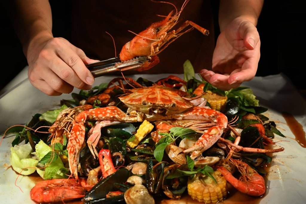 Hands reaching for a spread of dishes at the best halal seafood restaurant in Singapore