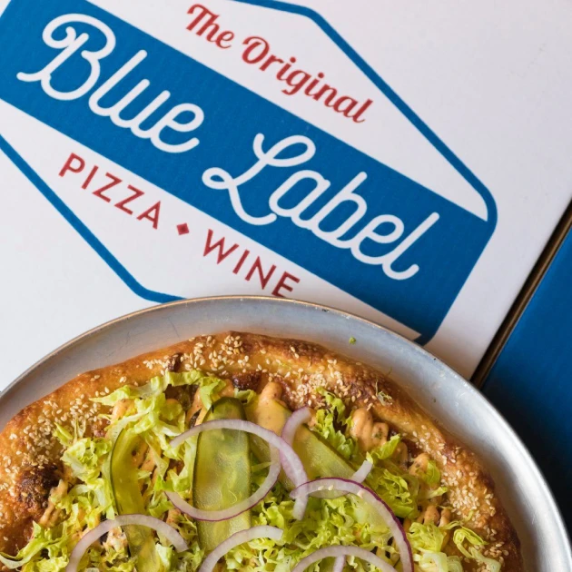 Blue Label pizza topped with shredded lettuce, pickles, red onion, and sesame seeds