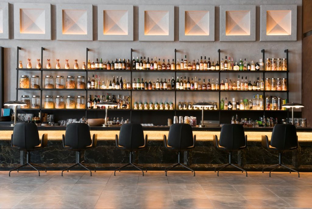 Modern bar counter with black swivel stools and illuminated liquor shelves